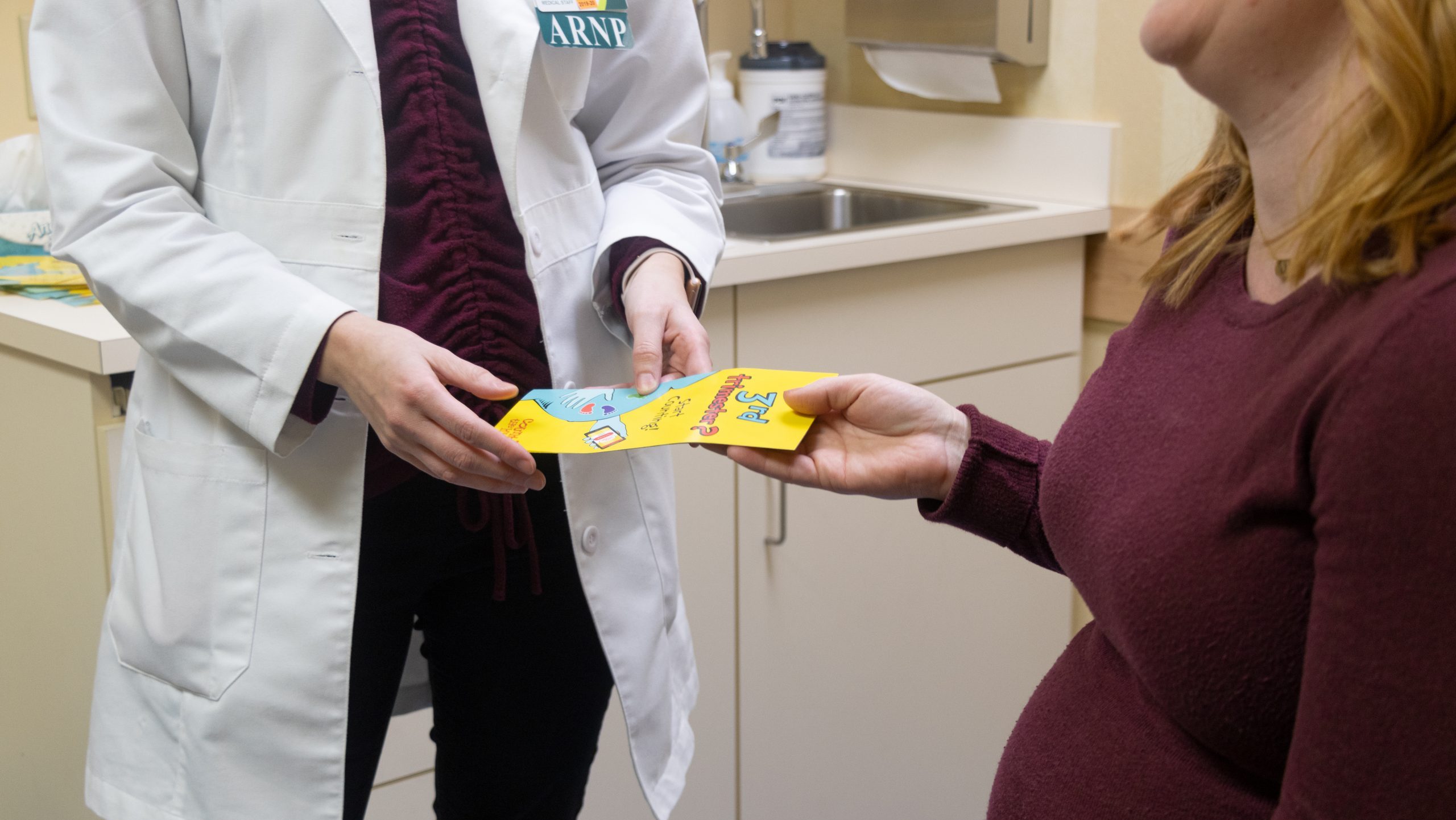 A midwife hands a Count the Kicks brochure to a pregnant woman during a prenatal visit.
