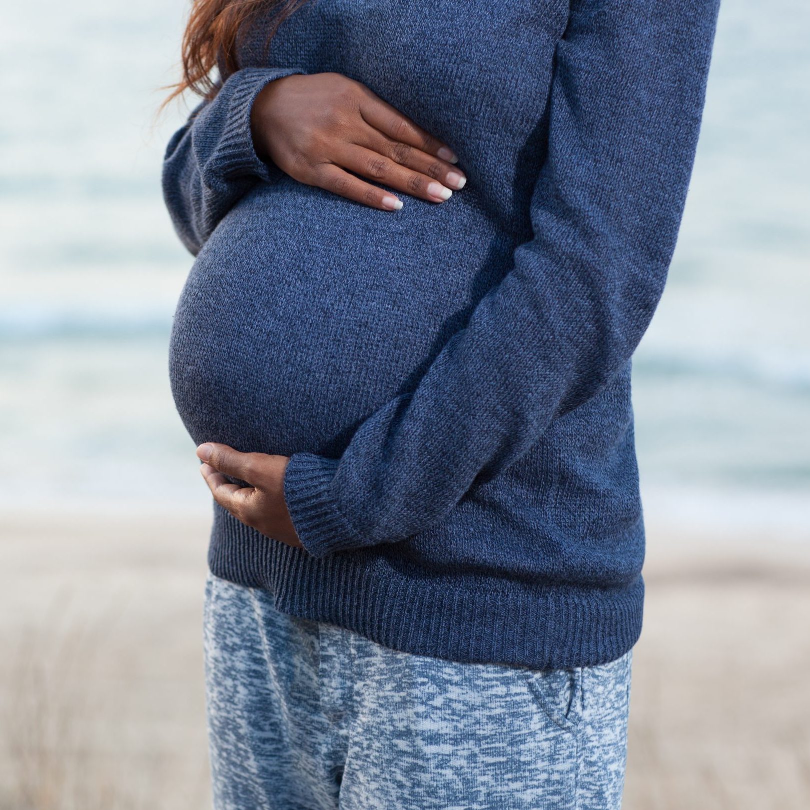 A pregnant woman wraps her hands around her baby bump.