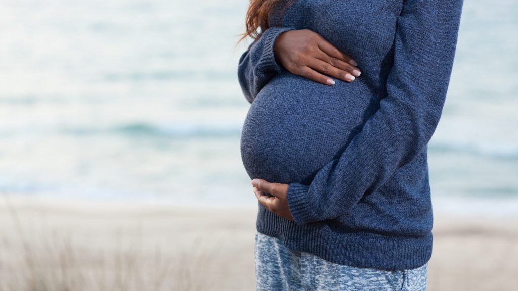 A pregnant woman rests her hands on her belly