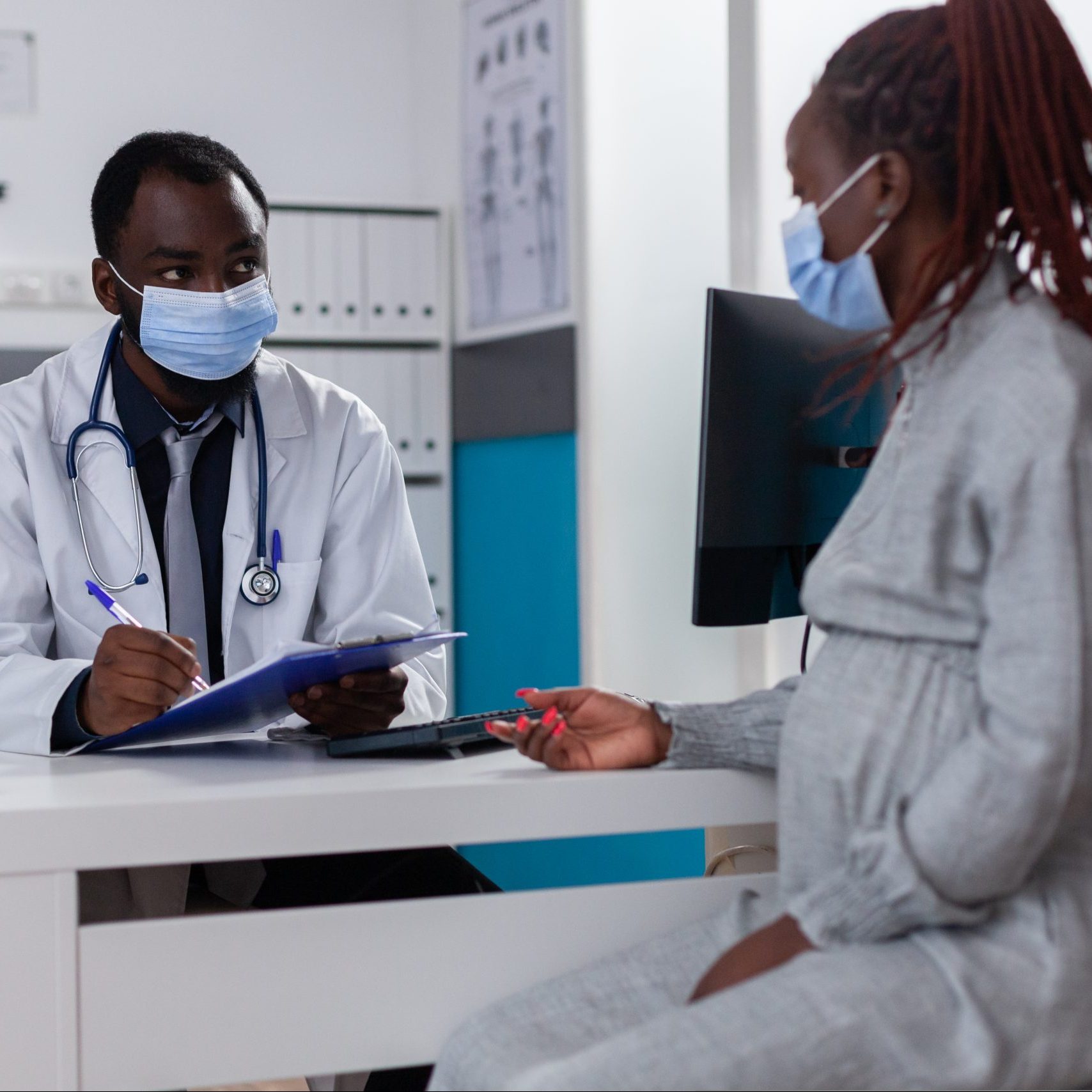 A Black pregnant woman talking to her doctor at an appointment.
