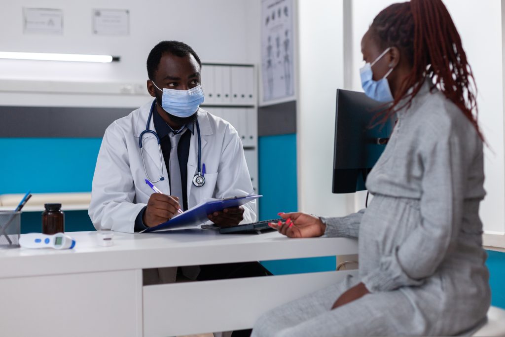 A Black pregnant woman talking to her doctor at an appointment.