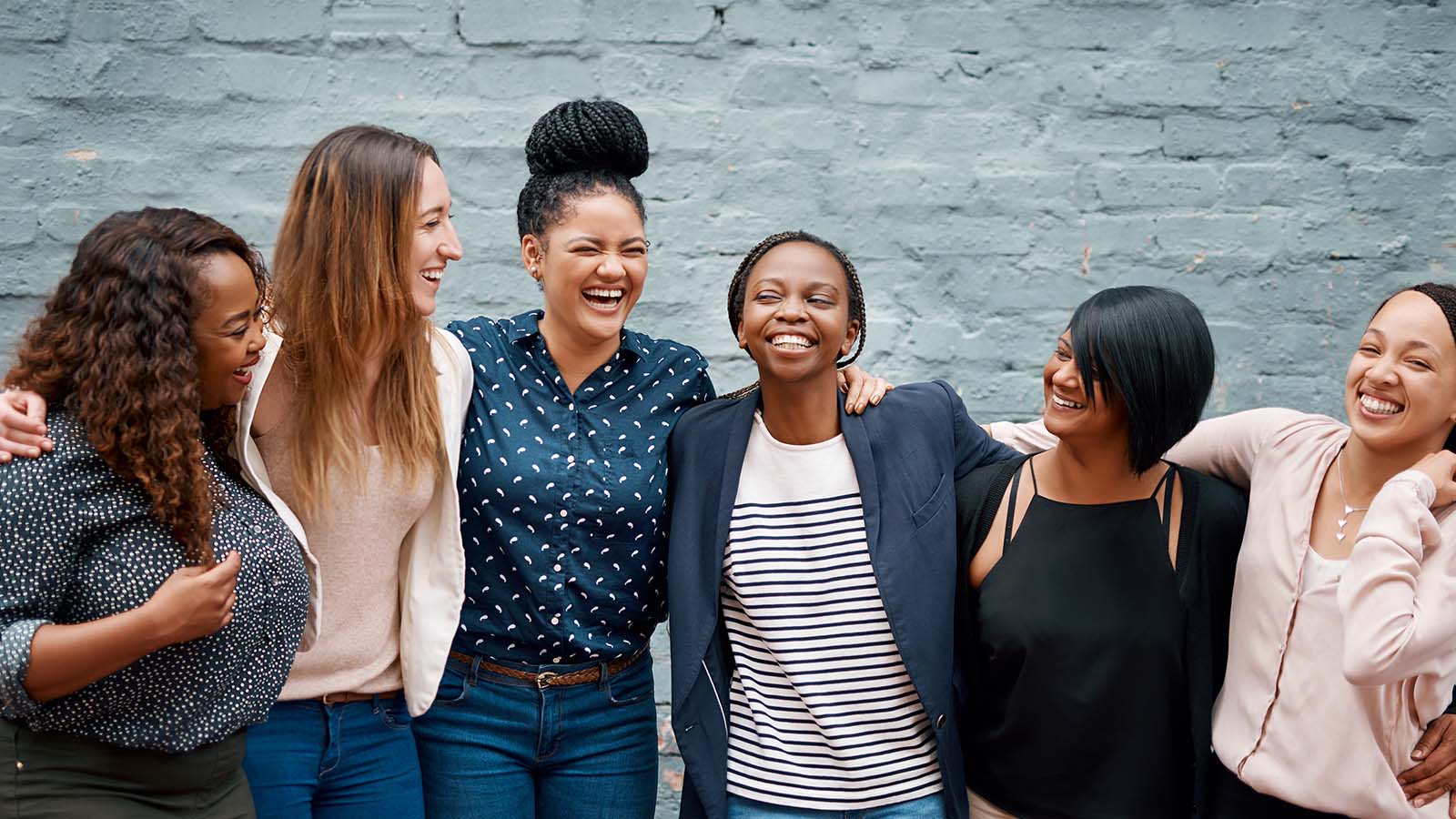 a diverse group of five women standing together in front of a blue wall