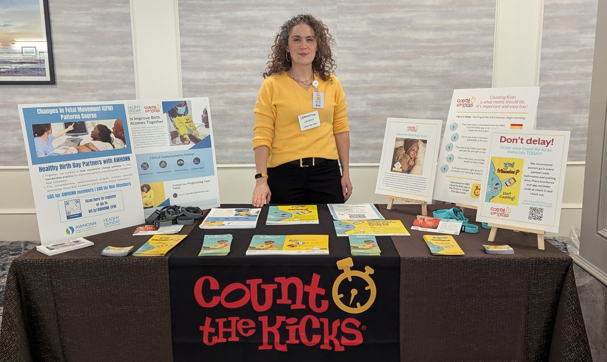 A Count the Kicks representative in a yellow shirt stands behind a table of Count the Kicks educational materials.